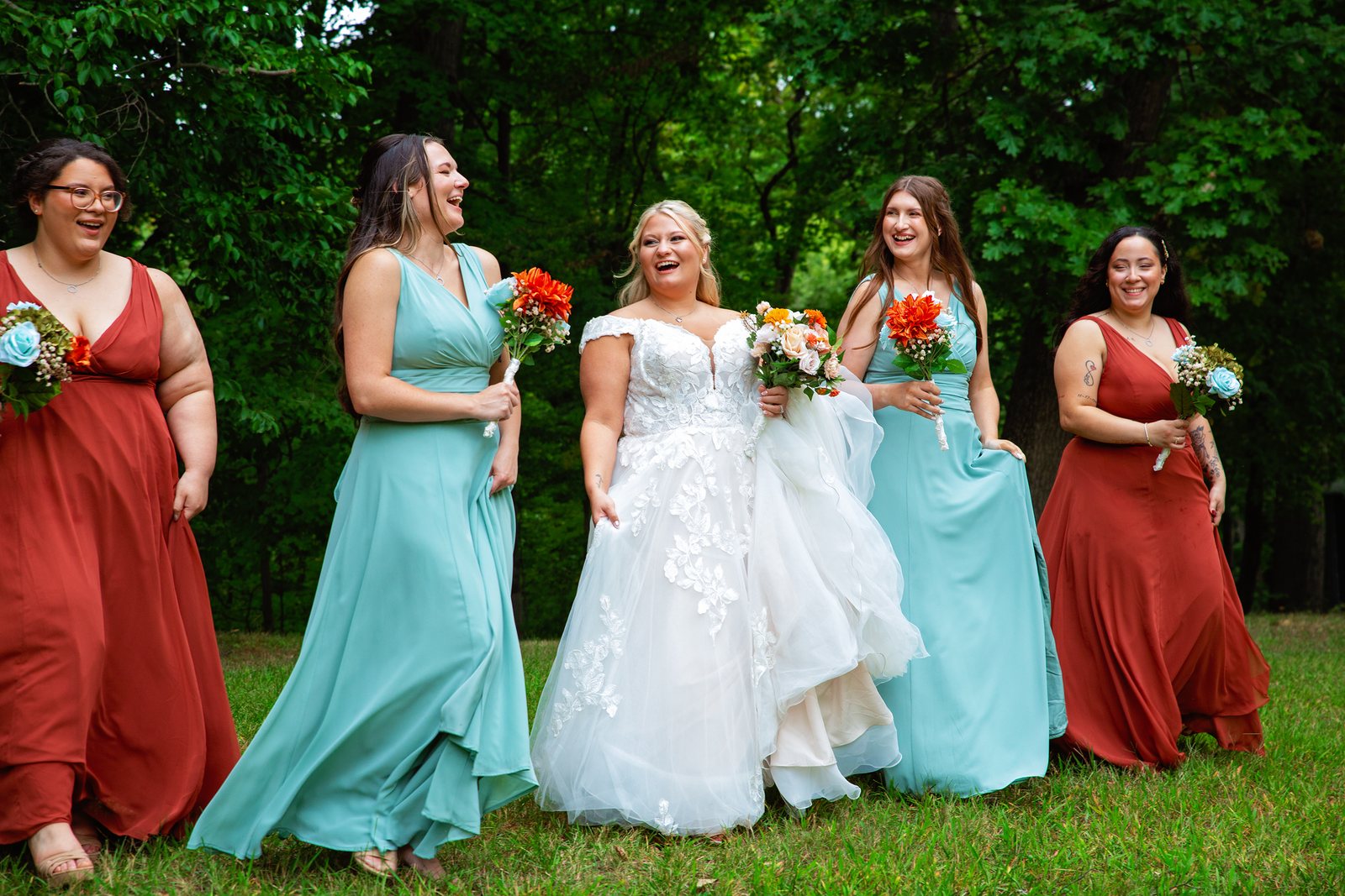 Bride laughing with her bridesmaids in teal dresses holding bright bouquets